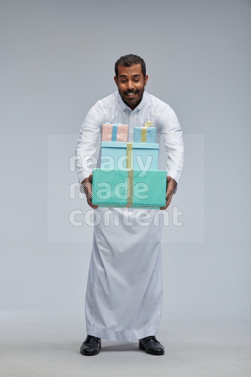Saudi man Wearing thob standing holding gift box on Gray background