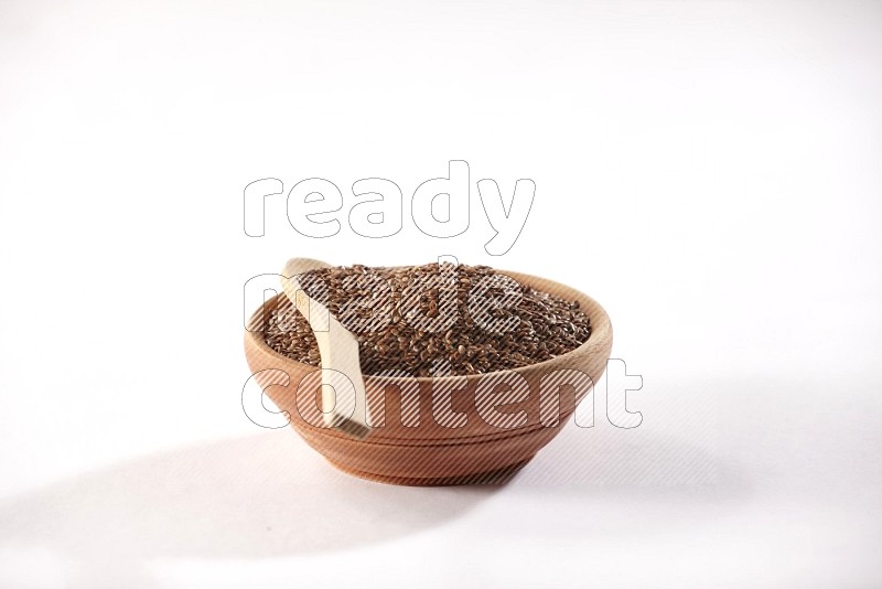 A wooden bowl full of flax seeds and a wooden spoon full of flax seeds in it on a white flooring