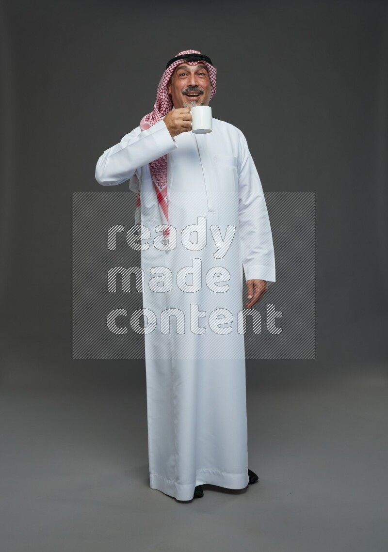 Saudi man with shomag Standing holding mug on gray background