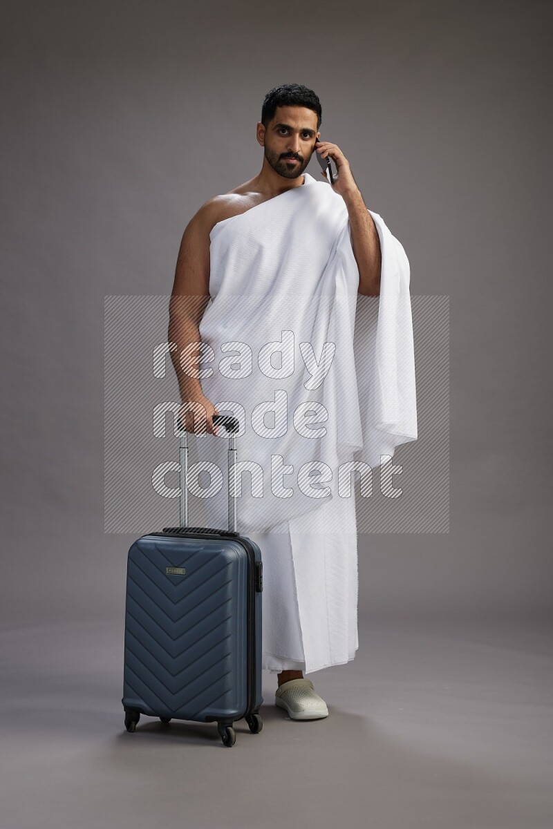 A man wearing Ehram Standing holding traveling bag on gray background