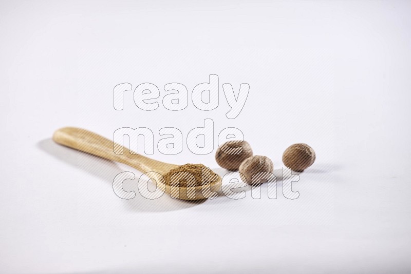 A wooden spoon full of nutmeg powder with nutmeg seeds beside it on a white flooring in different angles