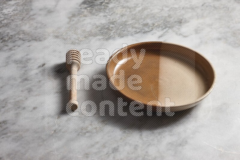Multicolored pottery oven plate with wooden honey dipper on the side on grey marble background