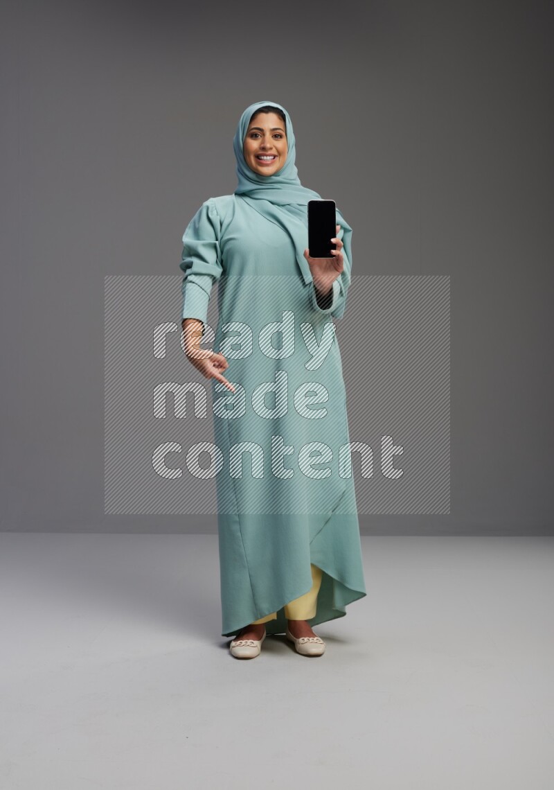 Saudi Woman wearing Abaya standing showing phone to camera on Gray background