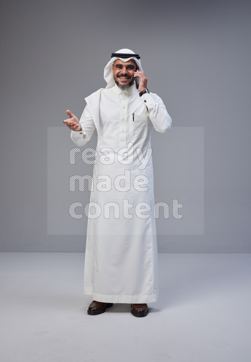 Saudi man Wearing Thob and white Shomag standing talking on phone on Gray background