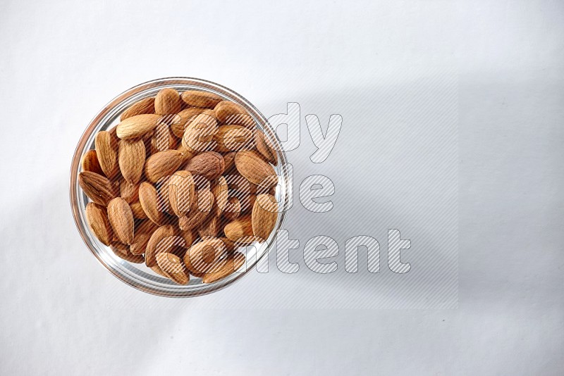 A glass bowl full of peeled almonds on a white background in different angles