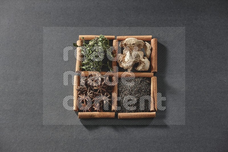 4 مربعات من عيدان القرفة ممتلئة بالشاي الأسود والزنجبيل المجفف والنعناع المجفف واليانسون النجمي على أرضية سوداء