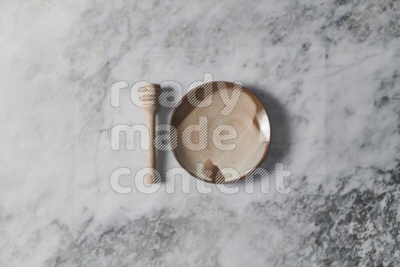 Multicolored pottery plate with wooden honey dipper on the side on grey marble background