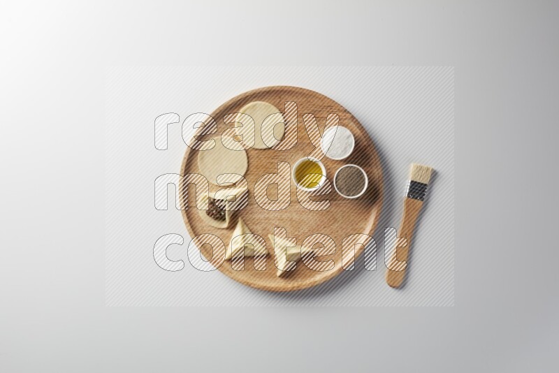 two closed sambosas and one open sambosa filled with meat while salt, black pepper and oil with oil brush aside in a wooden dish on a white background