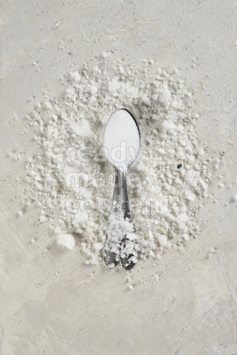 ملعقتان معدنيتان ممتلئتان بملح الطعام الناعم وملح الهايمالايا الناعم على خلفية بيضاء