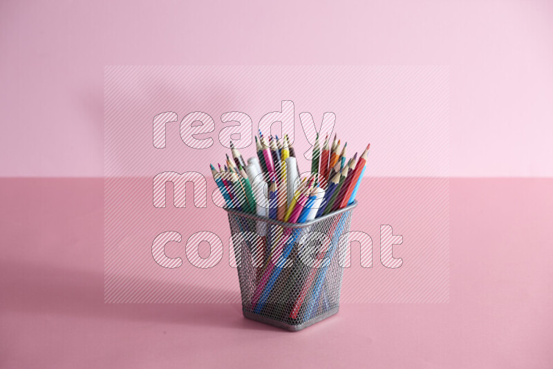 Pens, pencils and other different school supplies in a metal pen holder on rose background