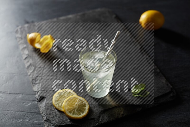 A glass of lemon juice with a straw on black background