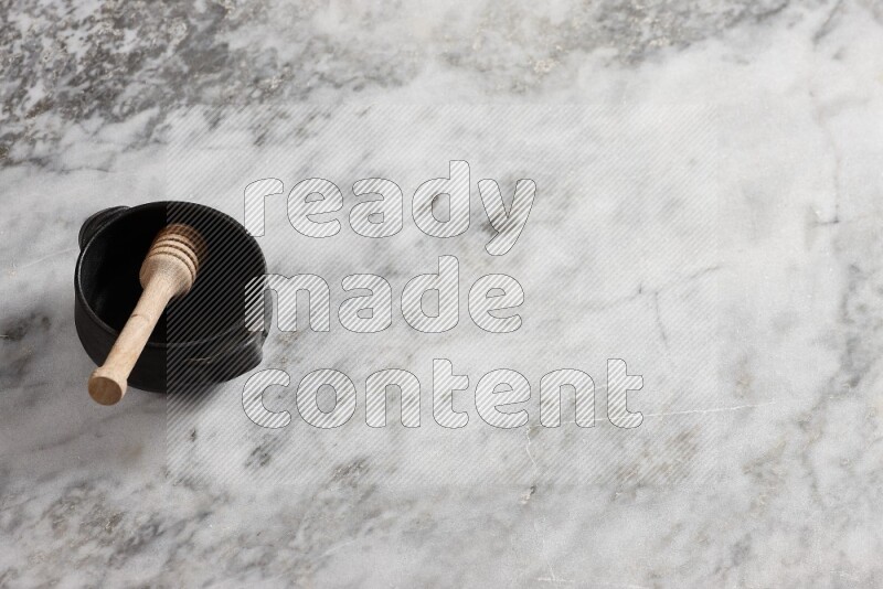Black pottery bowl with wooden honey dipper in it on grey marble background