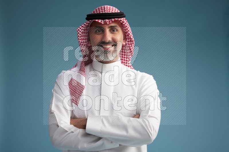 Saudi man wearing thob and shomagh posing to the camera on blue background