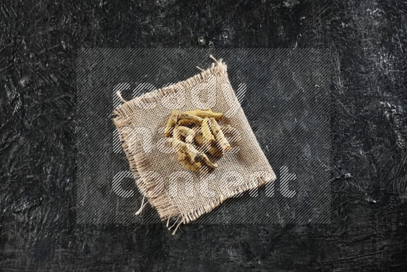 Dried turmeric whole fingers on a burlap piece of fabric on textured black flooring