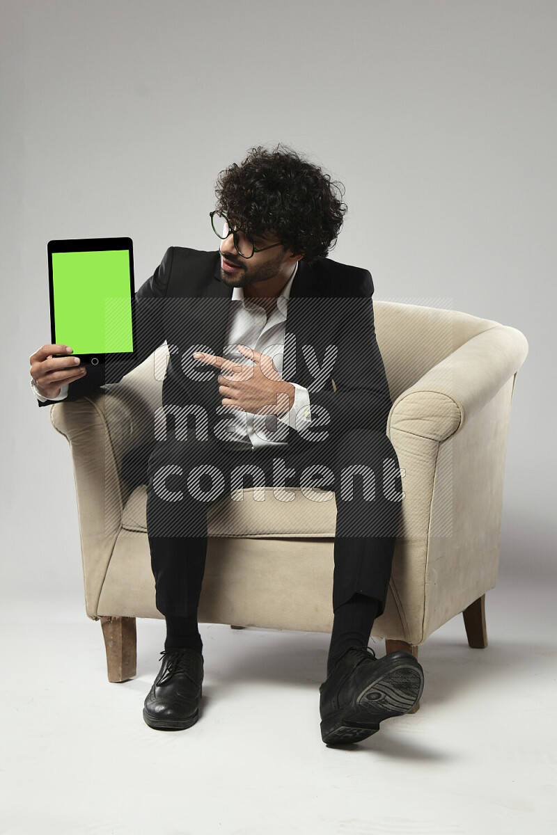A man wearing formal sitting on a chair showing a tablet screen on white background