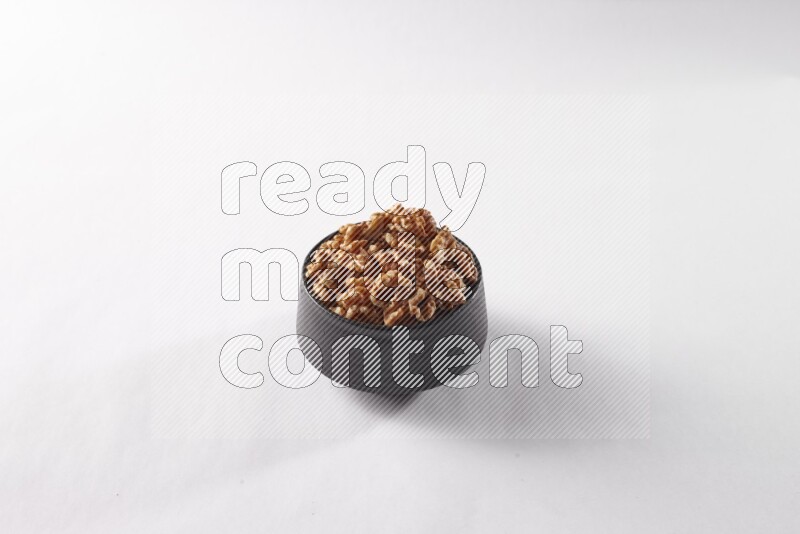 Walnuts in a black pottery bowl on white background