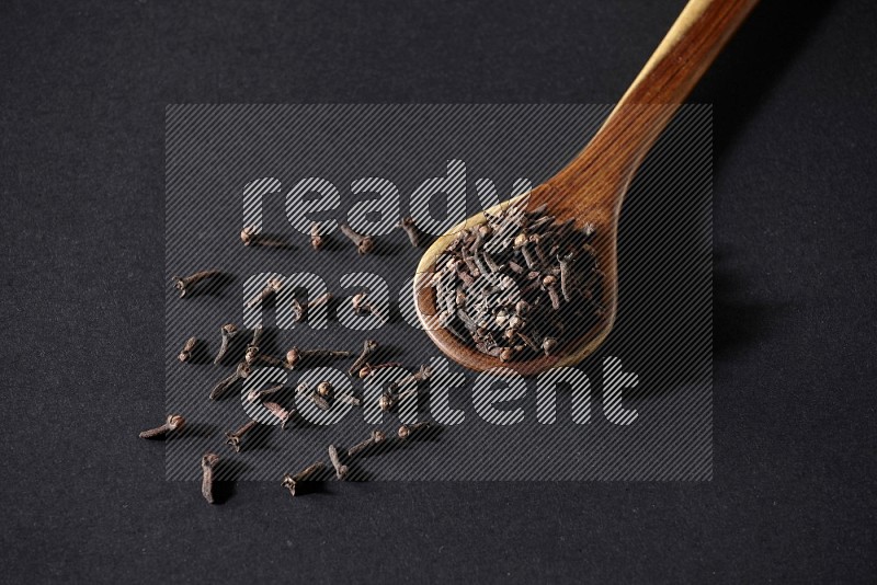 A wooden ladle full of whole cloves on a black flooring