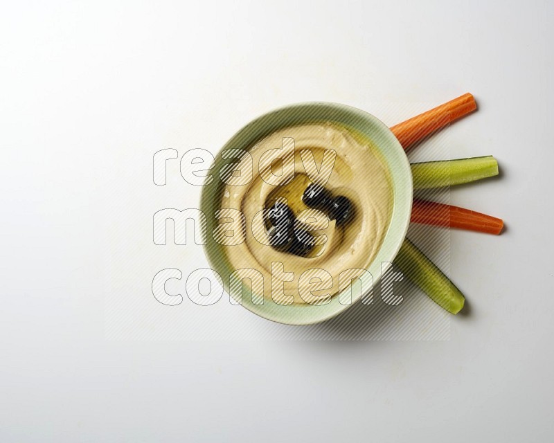 Hummus in a green plate garnished with black olives on a white background