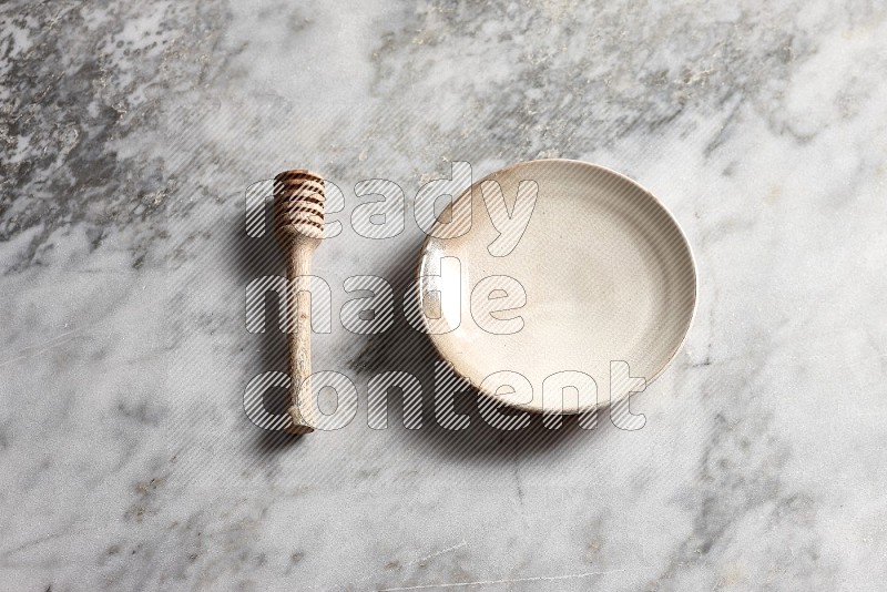 Beige Pottery Plate with wooden honey handle on the side with grey marble flooring, 65 degree angle
