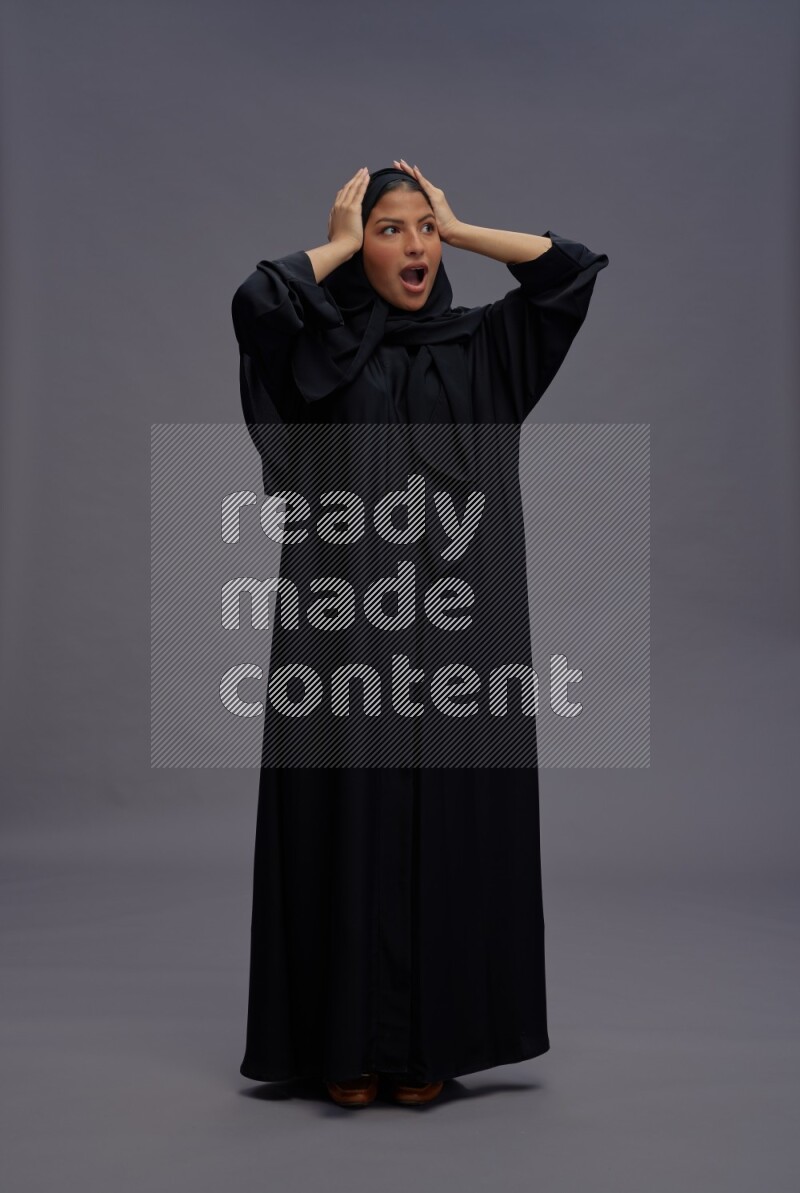 Saudi woman wearing Abaya standing hands behind head on gray background