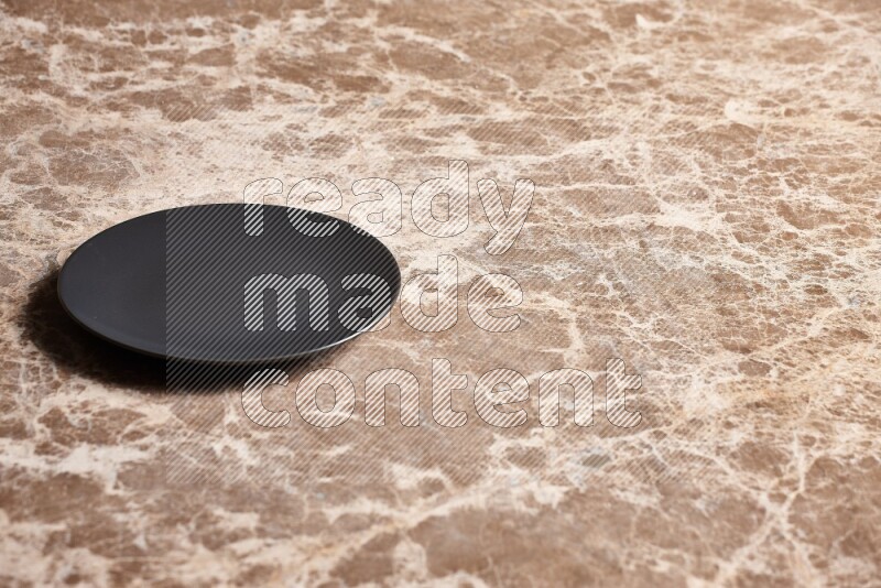 A black ceramic circular plate on beige marble background