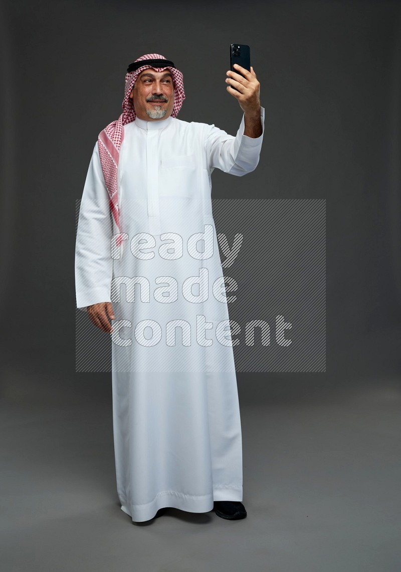 Saudi man with shomag Standing taking selfie on gray background