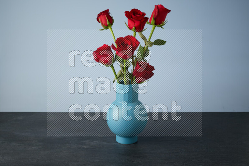 An arrangement of vivid red roses in a blue vase on black marble background