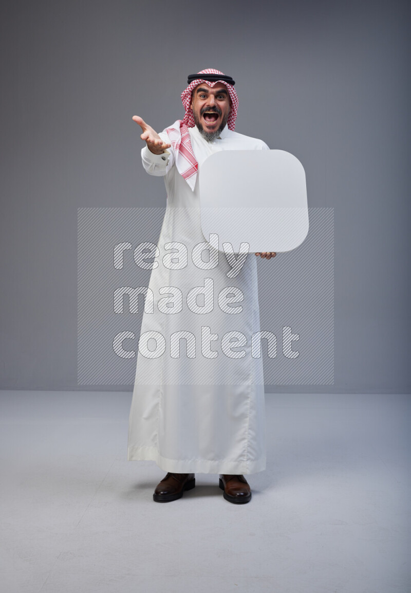 Saudi man Wearing Thob and red Shomag standing holding social media sign on Gray background