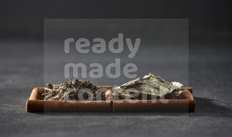 مربعان من أعواد القرفة ممتلئان بأوراق الغار والريحان المجفف علي خلفية سوداء