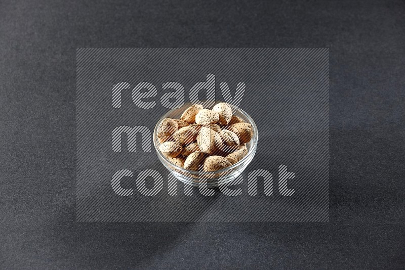 A glass bowl full of almonds on a black background in different angles