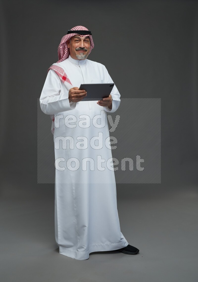 Saudi man with shomag Standing working on tablet on gray background