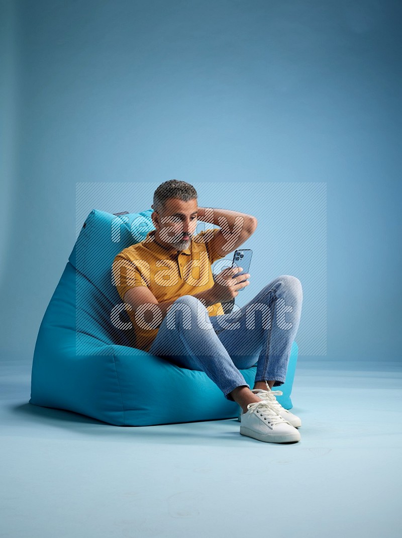 A man sitting on a blue beanbag and texting on phone