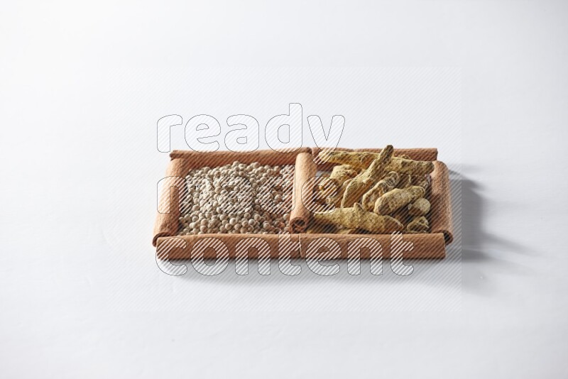 مربعان من أعواد القرفة ممتلئان بحبوب الفلفل الأبيض وأصابع الكركم علي خلفية بيضاء