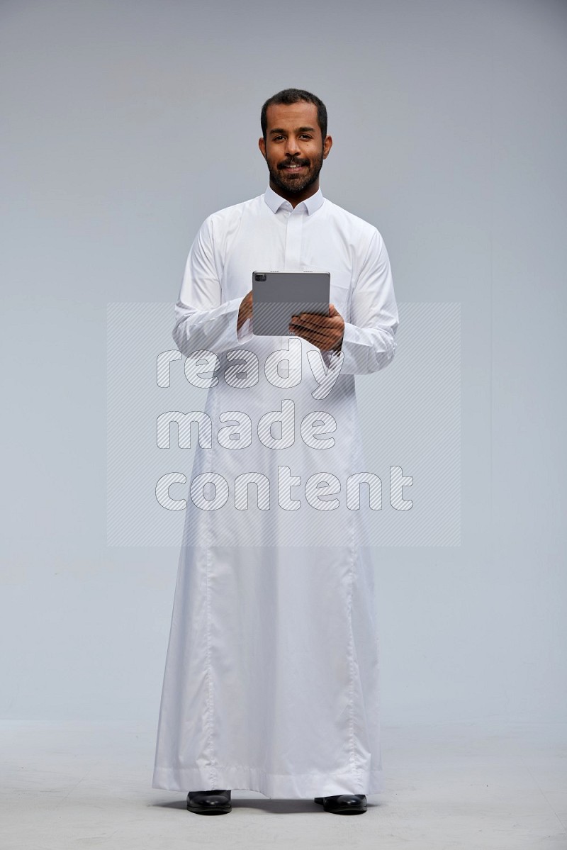 Saudi man wearing Thob standing working on tablet on Gray background