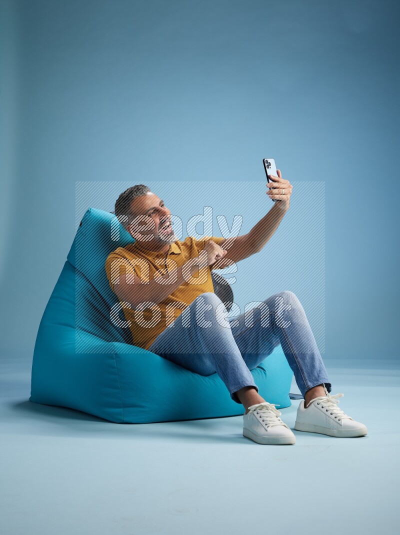 A man sitting on a blue beanbag and taking selfie