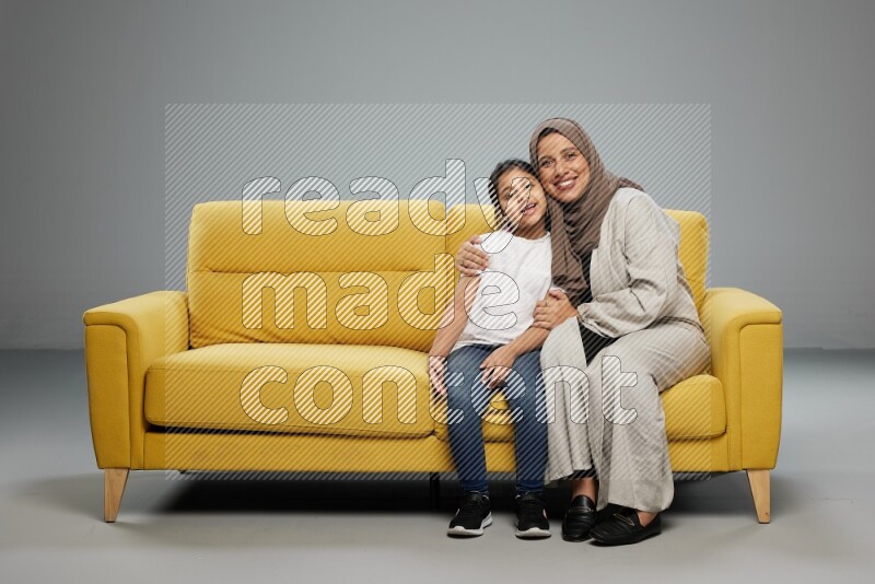 A girl with her mother sitting and interacting with the camera on gray background