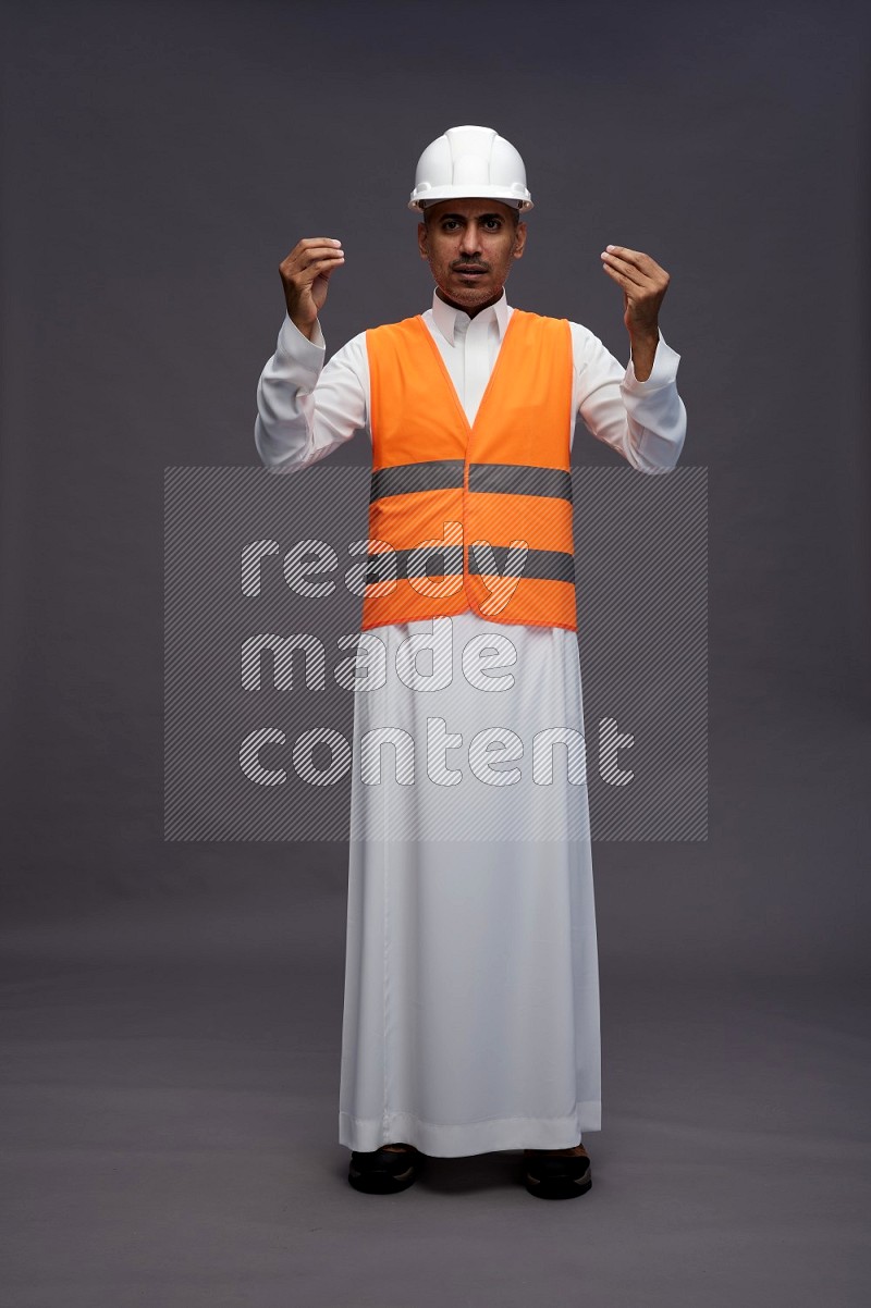 Saudi man wearing thob with engineer vest standing interacting with the camera on gray background