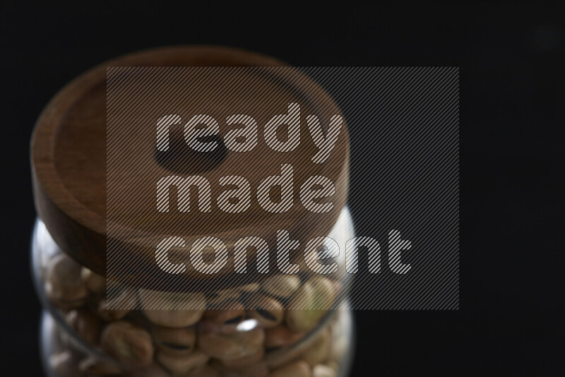 Fava beans in a glass jar on black background