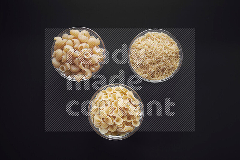 Different pasta types in glass bowls on black background