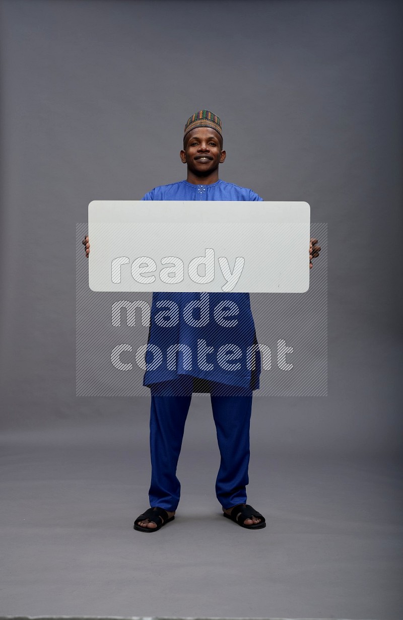 Man wearing Nigerian outfit standing holding board on gray background