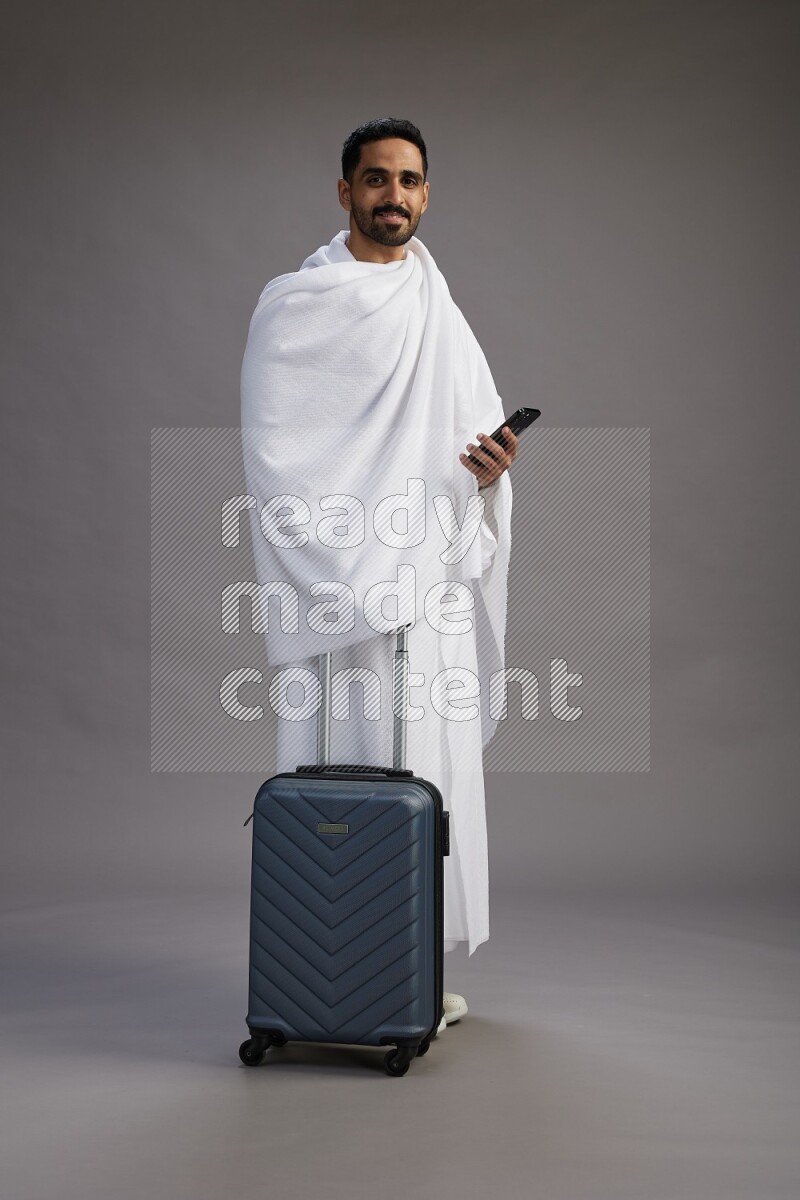 A man wearing Ehram Standing holding traveling bag on gray background