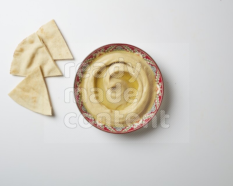Hummus in a red plate with patterns garnished with olive oil on a white background