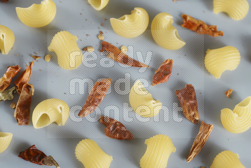 Raw pasta with different ingredients such as cherry tomatoes, garlic, onions, red chilis, black pepper, white pepper, bay laurel leaves, rosemary, cardamom and mushrooms on light blue background