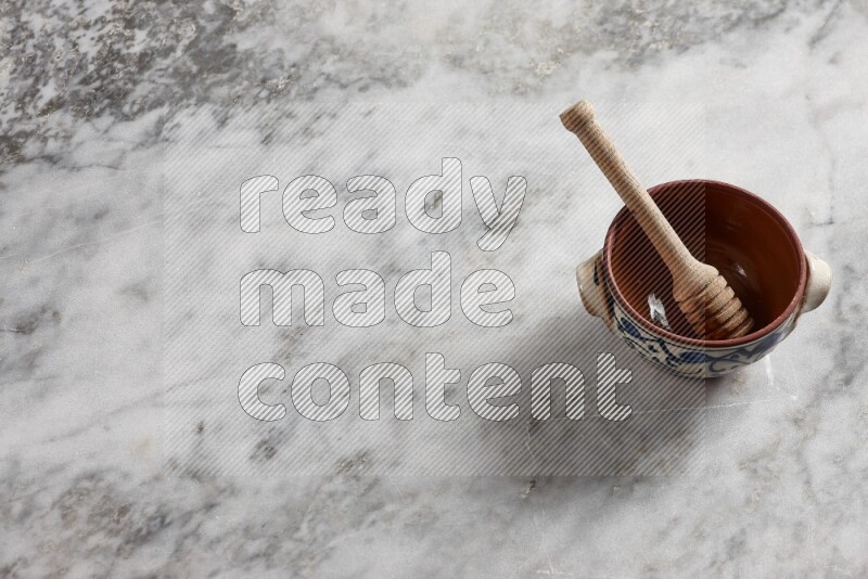 Decorative pottery pot with wooden honey dipper in it on grey marble background