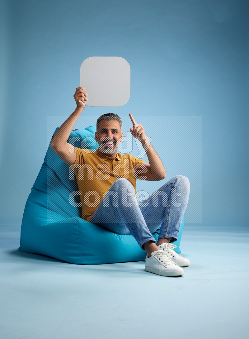 A man sitting on a blue beanbag and holding social media sign