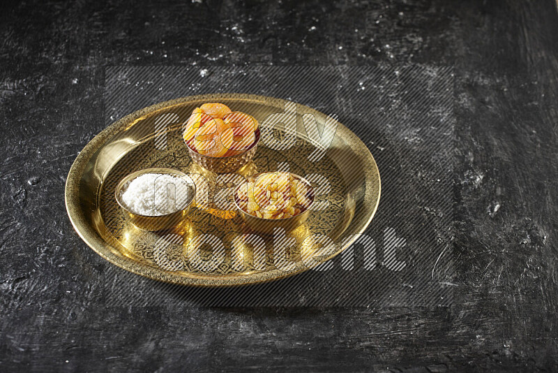 Dried fruits in metal bowls on a tray in a dark setup