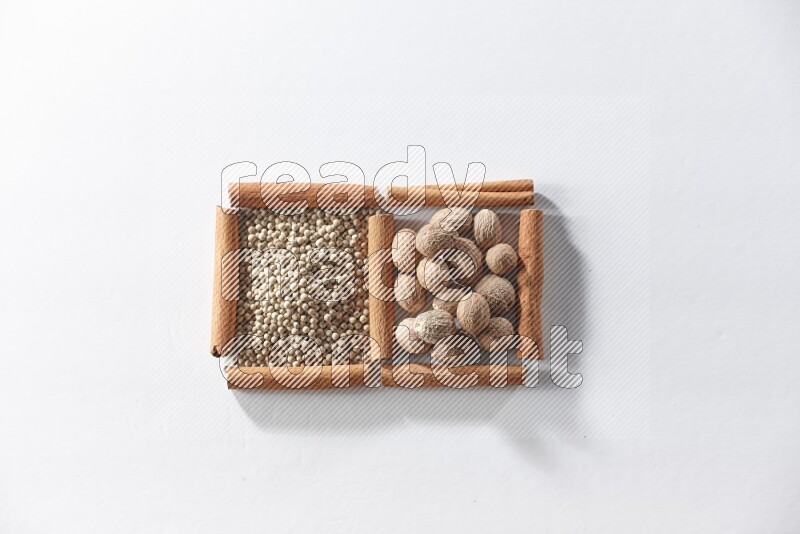 مربعان من أعواد القرفة ممتلئان بحبوب الفلفل الأبيض وجوزة الطيب علي خلفية بيضاء