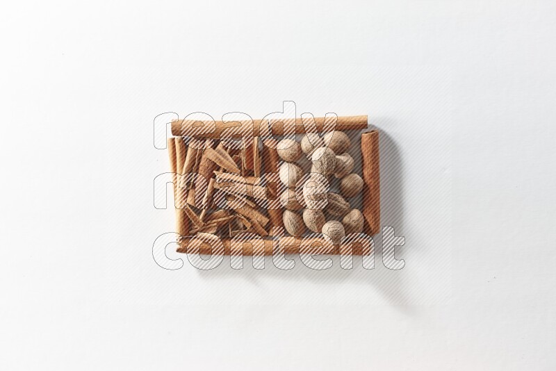 مربعان من أعواد القرفة ممتلئان بقطع من القرفة وجوزة الطيب علي خلفية بيضاء