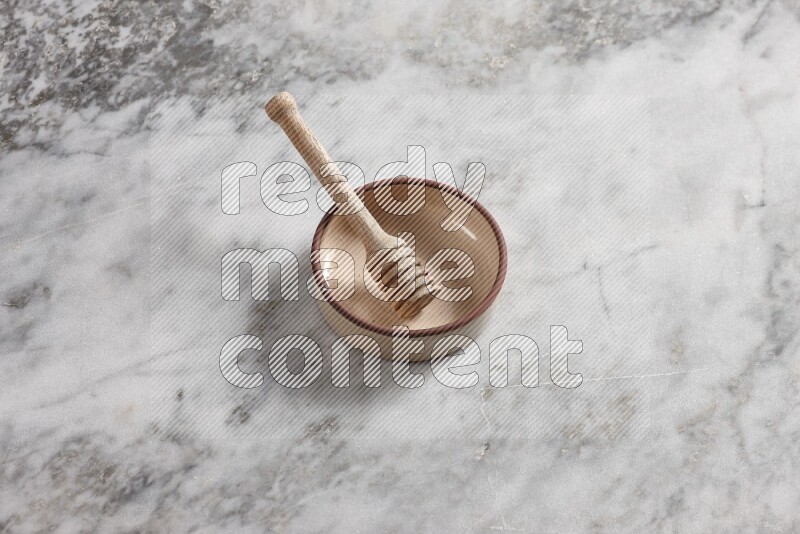 Beige Pottery oven bowl with wooden honey handle on the side with grey marble flooring, 65 degree angle