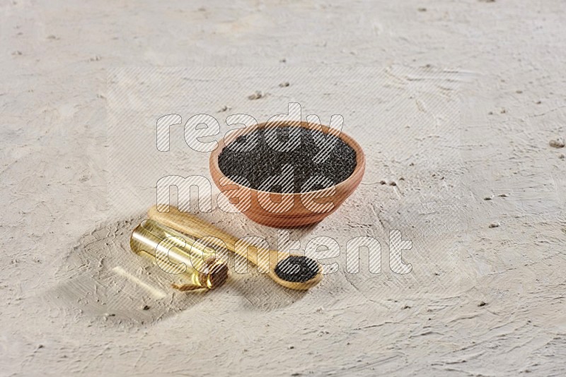 وعاء خشبي وملعقة مليئان ببذور حبة البركة مع زجاجة من زيت حبة البركة على أرضية بيضاء